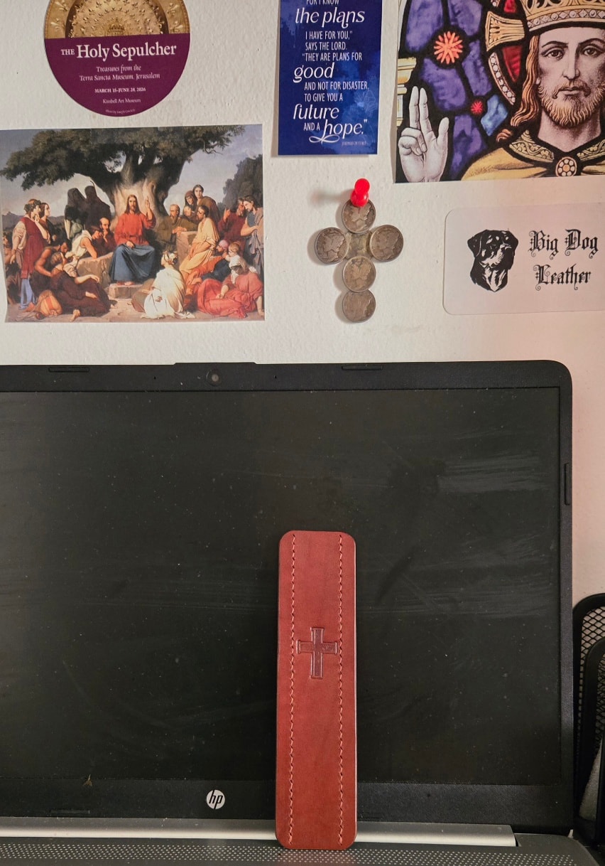 Bookmark propped against monitor — cross stamp face, workspace background