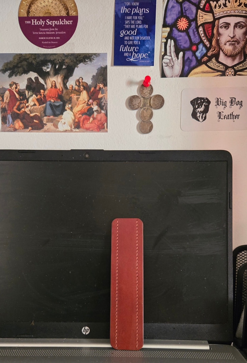 Bookmark propped against monitor — plain back face, workspace background